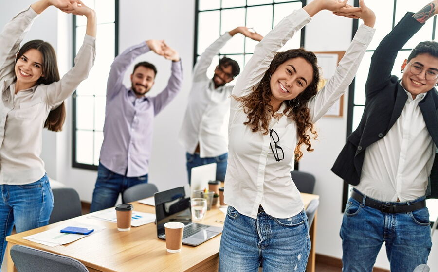 eine Gruppe junger Menschen im Büro die sich im Stehen strecken